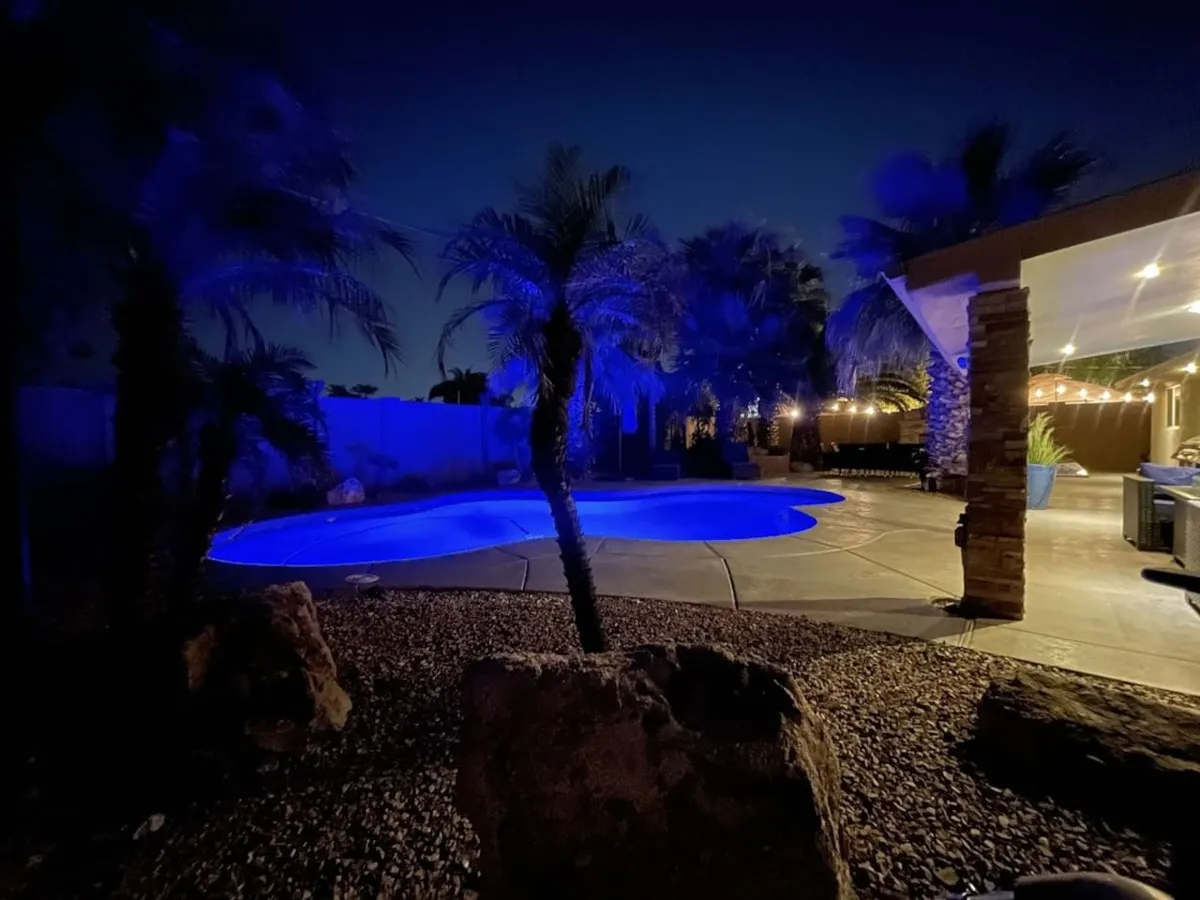 An inviting outdoor space with a beautifully illuminated swimming pool, stylish outdoor seating, palm trees, and festively lit landscaping. The mood is lively yet tranquil, ideal for evening gatherings or celebrations under the stars.