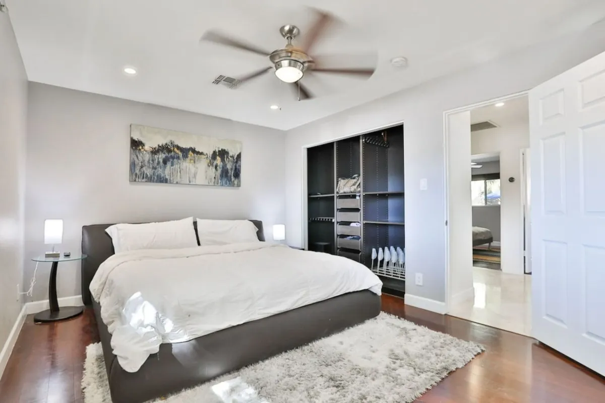 A sunlit bedroom featuring a cozy bed with comfortable linens, appealing artwork on the wall, and a spacious closet. The natural light and soft decor create a peaceful atmosphere, perfect for unwinding and rejuvenating.