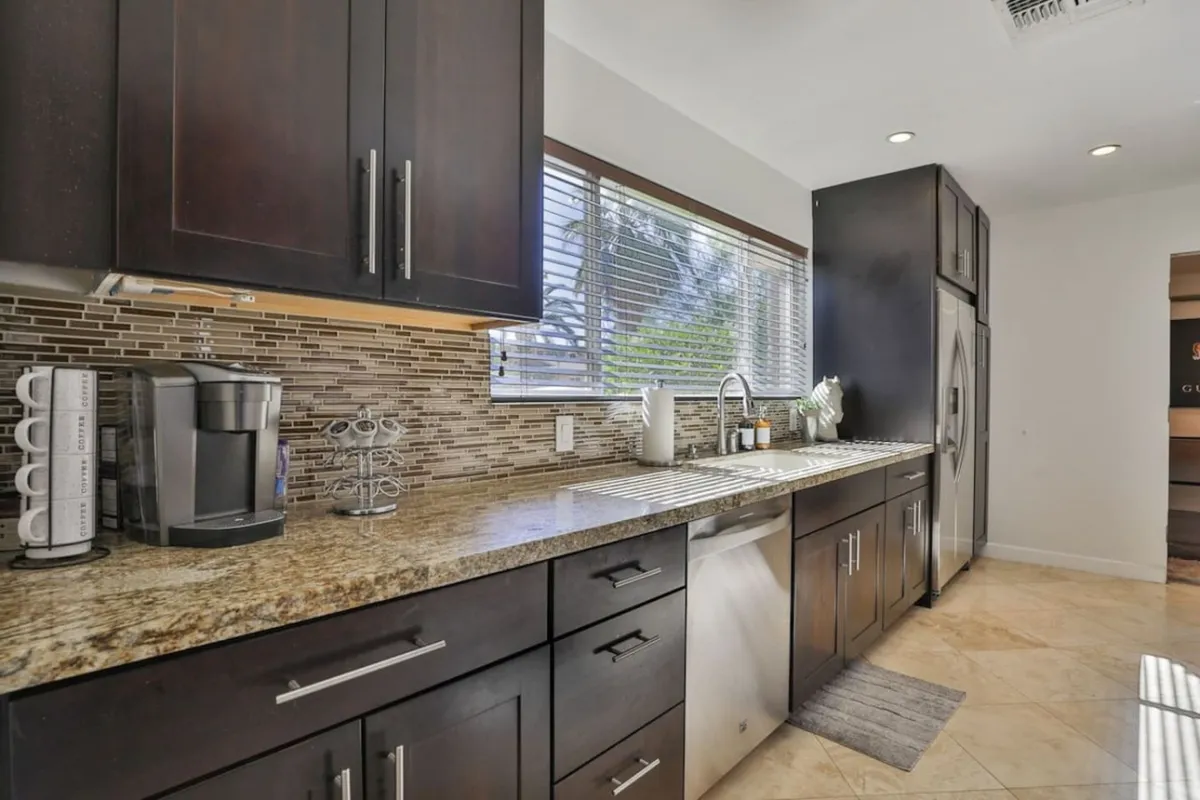 This kitchen is designed with dark cabinetry, a prominent granite countertop, stainless steel appliances, and a window that brings in natural light. The space feels warm and inviting, ideal for both everyday cooking and special gatherings.