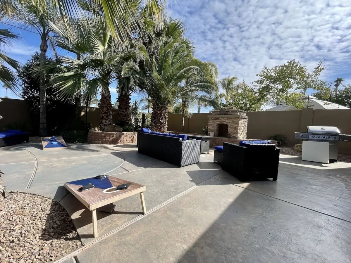 A beautifully arranged exterior setting featuring an outdoor seating area, grill, fireplace, and palm trees. The area is designed for barbecuing, social gatherings, relaxing, and outdoor dining, creating an inviting ambiance for al fresco meals with friends and family.
